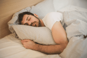 homme qui dort, il dort en serrant sa couette rayée beige et blanche